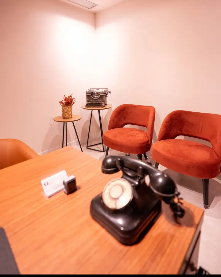 Mesa do consultório com telefone antigo e poltronas ao fundo